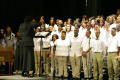 Primary view of [Choir members sing on stage while being directed by conductor]