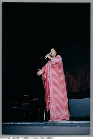 Primary view of object titled '[Full shot of Angela Bofill in a pink dress onstage]'.