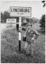 Photograph: [Junebug Clark leans on a sign for the city of Lynchburg, TN]