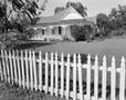 Photograph: [The exterior of a house with a white picket fence]