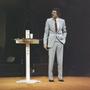 Photograph: [Televangelist Mike Evans giving a sermon in a grey suit with his han…