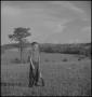Photograph: [Raymond standing in a field with a rifle]
