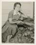 Photograph: [Dorothy Babb sitting on a wood pile with her dog]