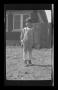 Photograph: [A young boy standing in front of a house]