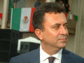 Photograph: [Carlos Garcia de Alba close-up with Mexican flags in background]