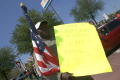 Photograph: [Man holding American flag and yellow handwritten sign]