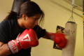 Photograph: [Young woman in red boxing gloves hitting heavy bag]