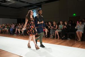 [Design student walking with male model down runway]