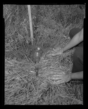 [Photograph of an individual uncovering a helicopter part in a field]