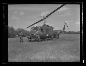 [Photograph of two soldiers standing by a UH-1B Iroquois helicopter in a field]