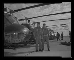 [Photograph of two men posing in front of a row of UH-1F Iroquois helicopters, 2]