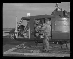 [Photograph of two individuals loading the cabin of UH-1B Iroquois helicopter]