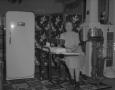 Photograph: [Portrait of a Woman Sitting Near a Refrigerator]