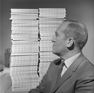 [Man sitting profile in front of large stack of books]