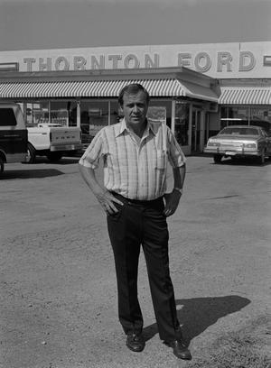 [Man standing in front of a Ford dealership, 3]