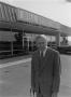 Photograph: [Man smiling in front of a Ford dealership]