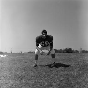 [Football player #68, Lennie Givens, in a wide stance leaning on his thighs]