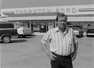 [Man standing in front of a Ford dealership, 2]
