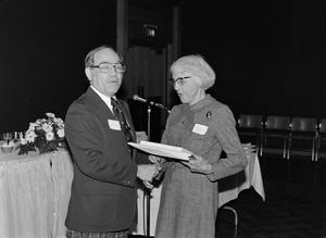 [Woman receiving items from man at microphone]