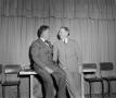 Photograph: [Two men in suits sit on a table]