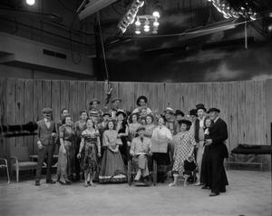 [Group of actors posing on set]