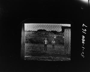 [Two men standing next to a shed in a field]