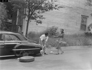[Woman helps man with car jack]