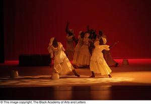 [Photograph of women in white dresses performing a dance on stage]