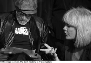 [Photograph of Melvin Van Peebles talking to a woman on stage]