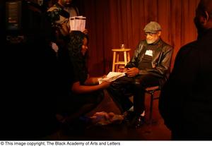 [Photograph of individuals gathered around Melvin Van Peebles on stage]