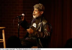 [Photograph of Melvin Van Peebles as he talks into a microphone on stage]