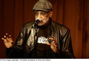 [Photograph of the director Melvin Van Peebles sitting in front of a microphone]