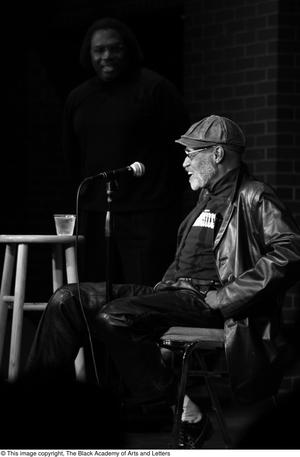 [Photograph of Melvin Van Peebles sitting in a chair on stage at 24-Hour Film Feast]