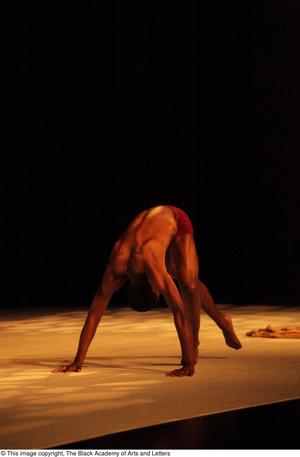 [Photograph of a dancer bending down to touch the stage]