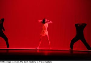 [Photograph of three dancers performing on a stage lit with red lights]
