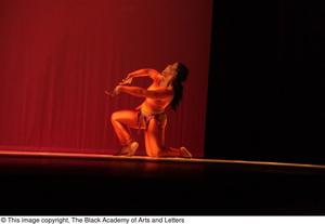 [Photograph of a woman kneeling on stage in an orange leotard]