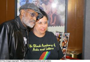 [Photograph of Melvin Van Peebles with a woman wearing a TBAAL shirt]
