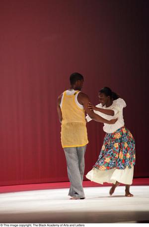 [Photograph of a woman and man dancing close together on a stage]