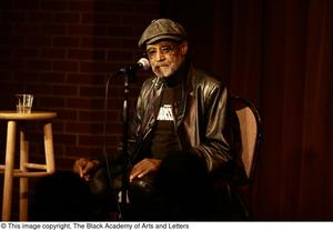 [Photograph of director Melvin Van Peebles sitting in a chair on stage]