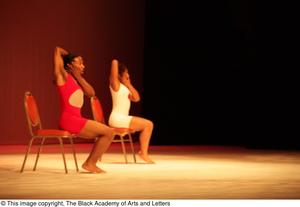 [Photograph of two dancers performing in chairs on stage]
