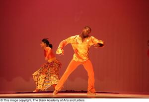 [Photograph of two dancers on a stage in orange outfits]