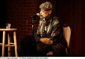 [Photograph of Melvin Van Peebles sitting in a chair on a stage]