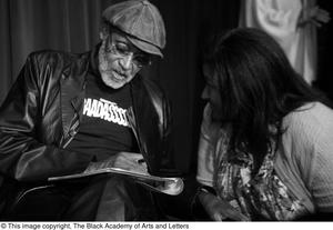 [Photograph of Melvin Van Peebles signing a book for a woman]
