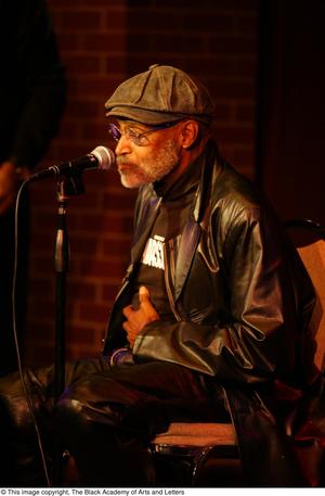 [Photograph of Melvin Van Peebles sitting in a chair on stage at a film festival]