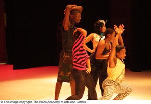 [Photograph of five dancers close together on a stage during a performance]