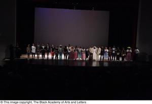 [Photograph of many dancers lined up on stage inside a dark auditorium]
