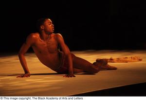 [Photograph of a man lying on stage during a dance performance]