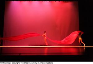 [Photograph of two individuals dancing on stage with a long piece of fabric]