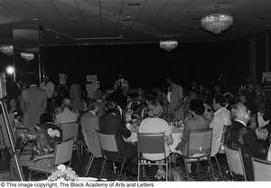 [Photograph of the backs of unidentified guests sitting at various dining tables]