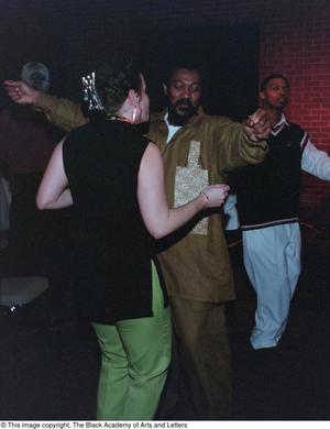 [Ras Tumba dancing with unknown woman with unknown man in background]